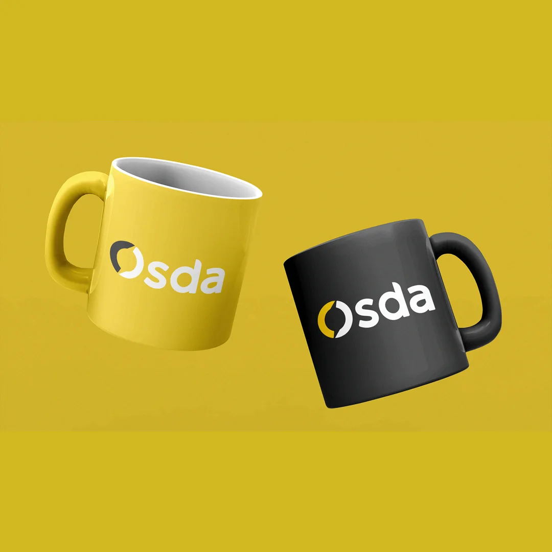 Mockup de duas canecas sobre fundo mostarda, uma amarela e uma grafite, ambas com a assinatura Osda aplicada em branco.