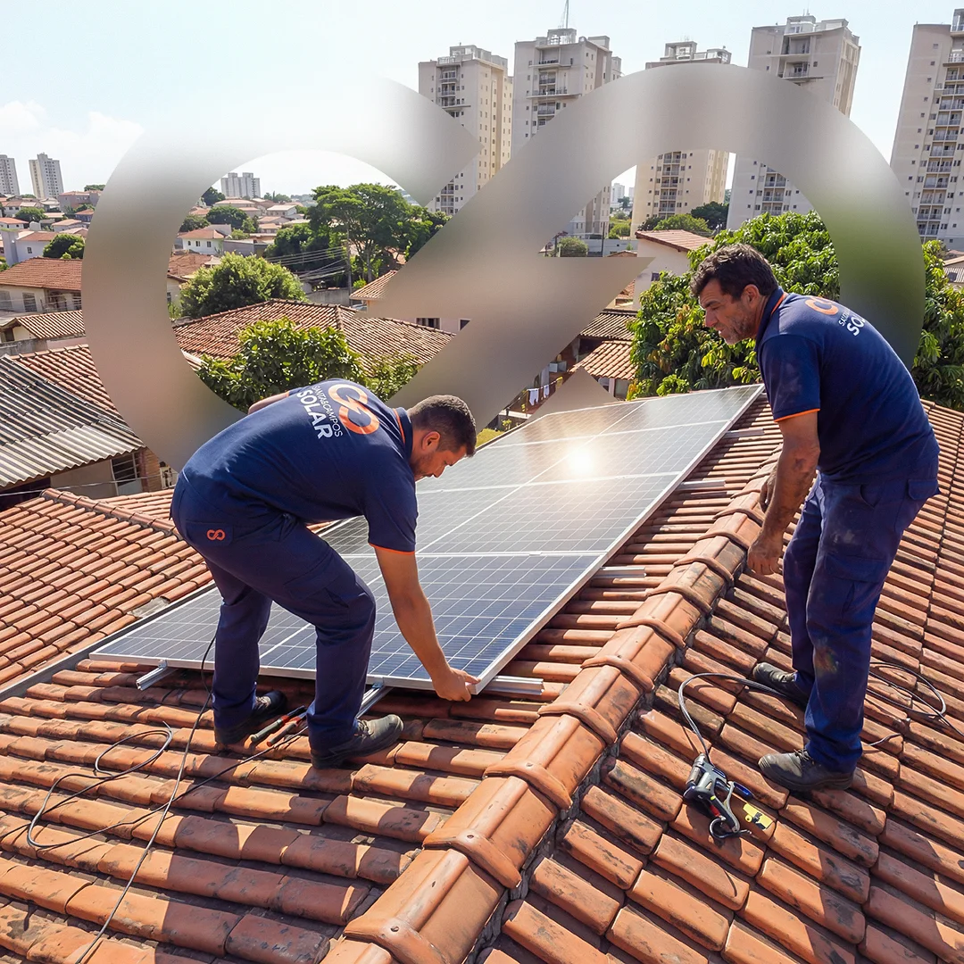 Dois técnicos de uniforme azul-marinho com detalhes laranja posicionam um módulo fotovoltaico sobre um telhado de telha cerâmica, com prédios ao fundo. Peça sem texto, apenas o monograma aplicado como marca d'água translúcida.