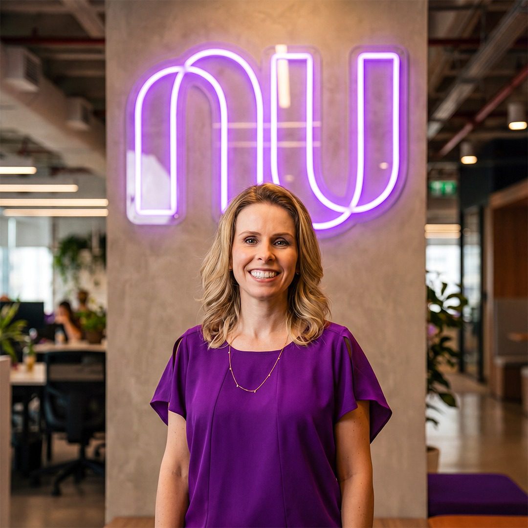 Smiling woman in a purple blouse stands in an office with a purple neon sign behind her